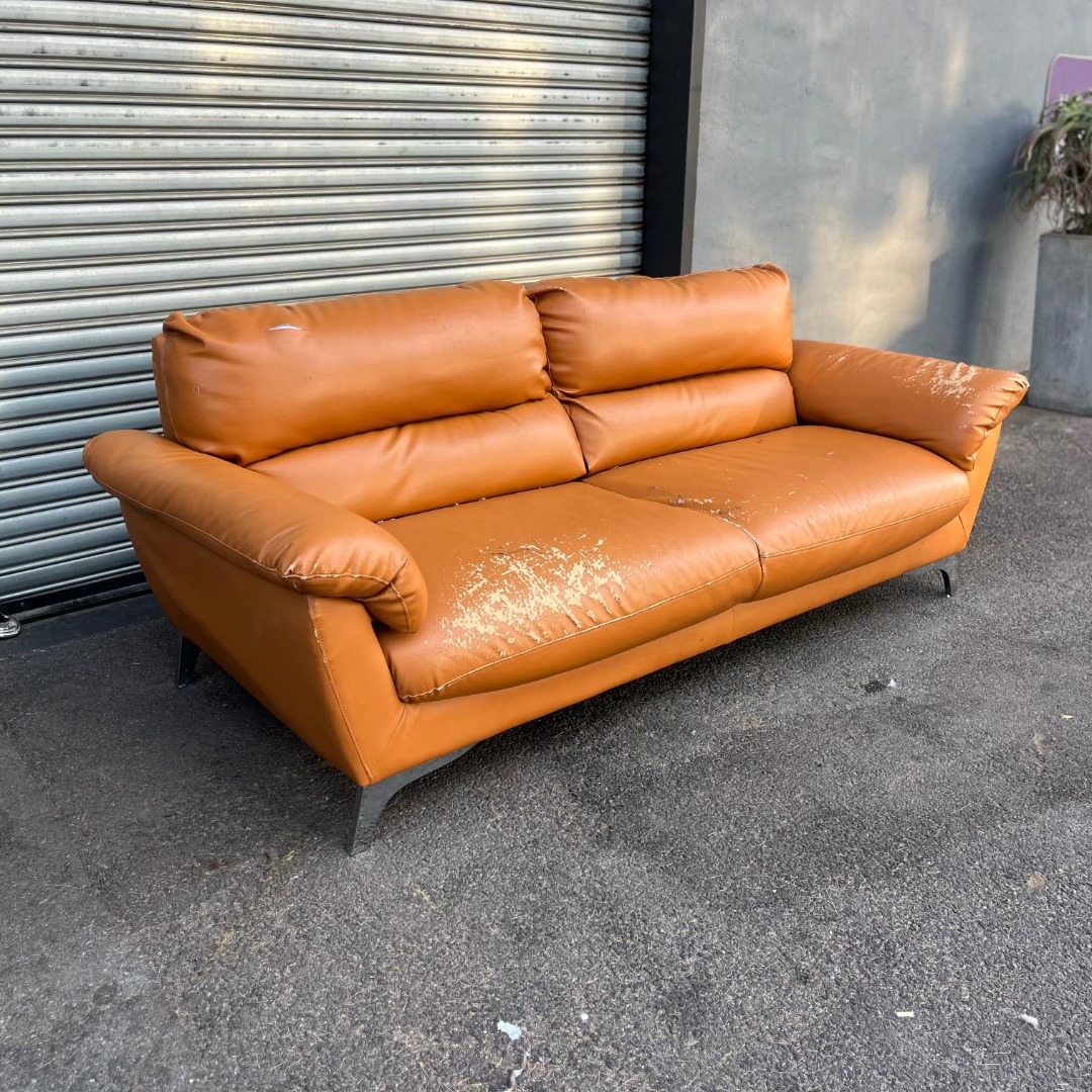 The original worn tan leather couch with peeling and scuffs, before reupholstery